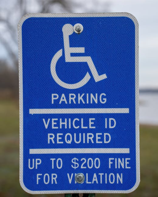 A blue rectangular parking sign with a white wheelchair symbol at the top indicating designated accessible parking. Below the symbol, the sign reads 'PARKING' in bold white letters, followed by smaller text stating 'VEHICLE ID REQUIRED' and 'UP TO $200 FINE FOR VIOLATION' separated by horizontal white lines. The sign is mounted on a grey pole in an outdoor setting, with a background of cloudy sky and a grassy area, relevant to house removals and relocation services, highlighting accessible parking regulations near a property in Hammersmith as part of home relocation logistics. The sign is associated with operations by Removal Companies Hammersmith, ensuring compliance with parking and access advice during the moving process.